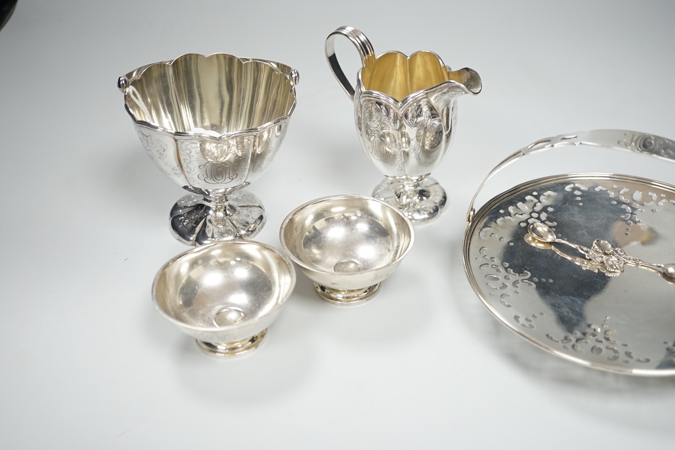 A sterling sugar basket, diameter 9.9cm, a sterling shallow basket dish, sterling cream jug and pair of sterling salts with spoons, 20.6oz.